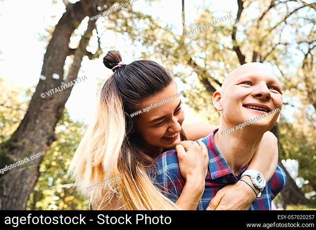 Close up image of young couple having fun and laughing in park at summer day. Boyfriend carrying his girlfriend on back. Happy moments together