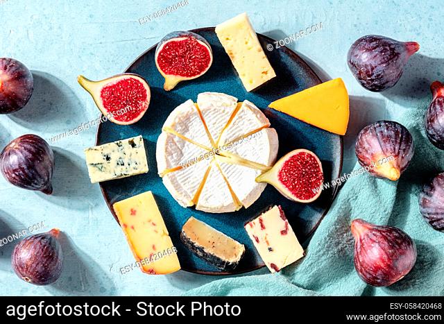 Many different cheeses on a plate, shot from the top with fresh figs, a flatlay on a blue background