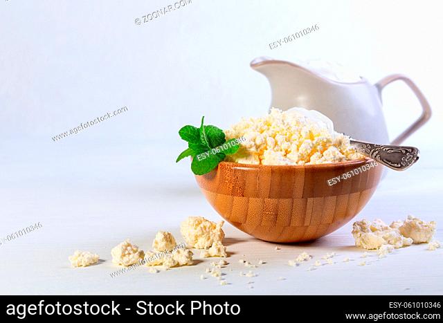 Organic cottage cheese is served in a wooden bowl with a spoonful of fresh sour cream. Concept of healthy eating. Copy the space