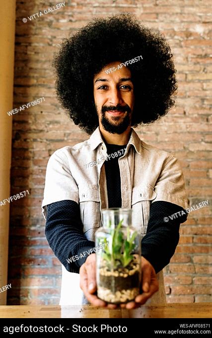 Smiling male gardener holding glass jar with succulent plant