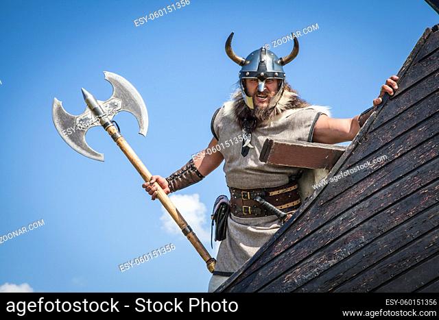 Strong Viking on his ship. Angry man holding historical axe weapon on ship looking at camera. isolated on sky background