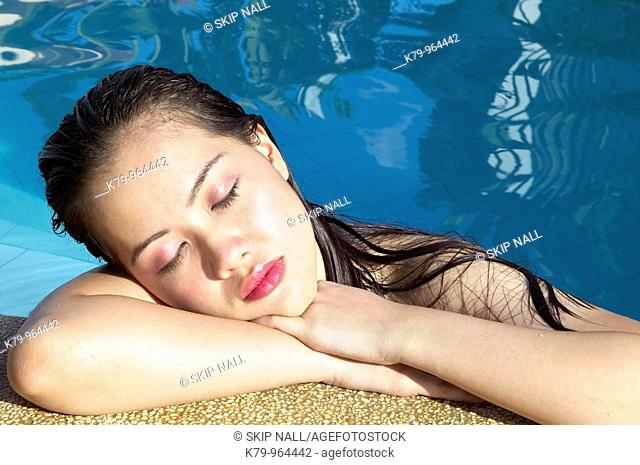 Pretty Asian young woman relaxing in swimming pool with eyes closed