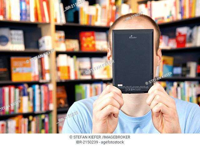 Man holding an electronic book or e-book reader, in front of his face, in a bookstore in Regensburg, Bavaria, Germany, Europe