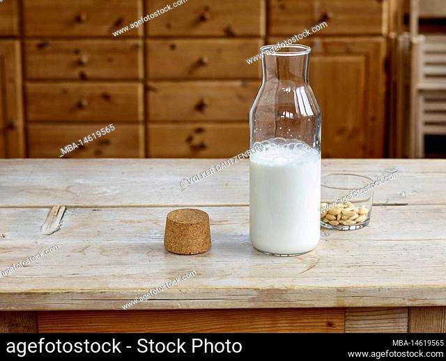 Steps for making almond milk, finished almond milk in a glass bottle with cork and a glass bowl with blanched almonds on a wooden table