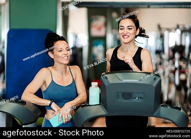 Sportswoman exercising on treadmill while female friend standing by her at gym