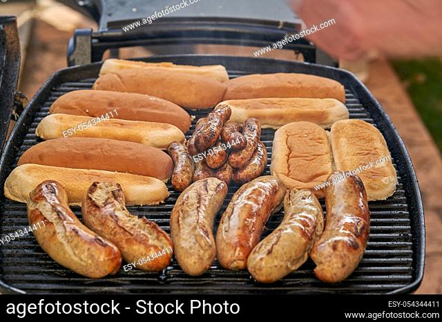 Grilled sausage on the burning grill. BARBECUE. Outdoor barbecue. Hot dogs sausages and breads on hot plate. Barbecue Picnic