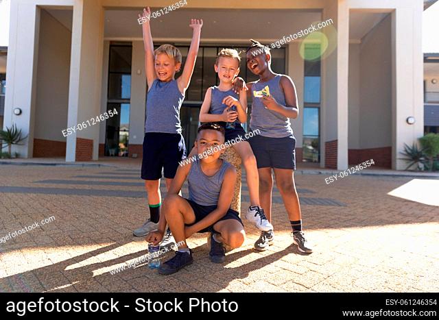 Cheerful elementary schoolboys against school building during sunny day