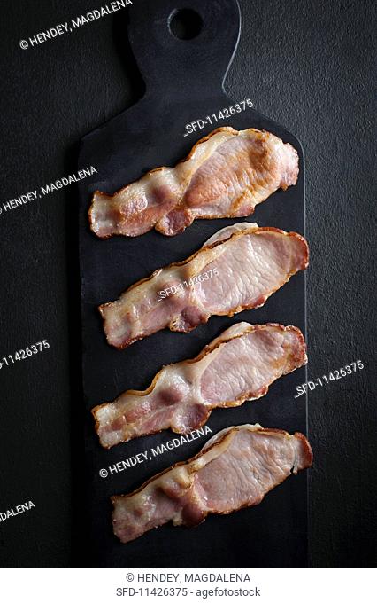 Four rashers of bacon on a black slate platter
