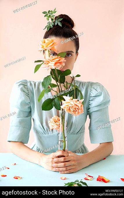 Young woman holding rose vase against pink background