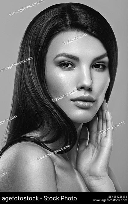 beautiful young woman with natural glowing makeup and long straight hair. beauty shot on gray background. hand touching face. copy space