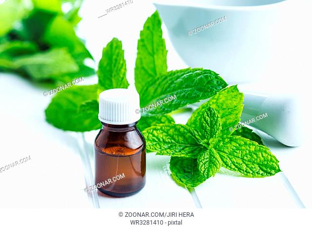 Bottle of essential mint oil and mint leaves