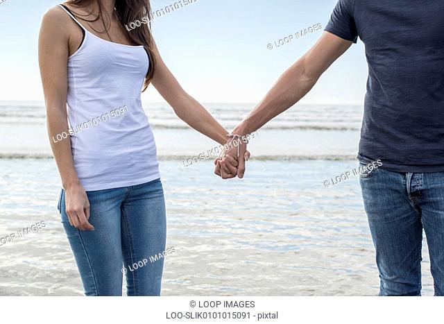 A young couple walk holding hands across the beach at Porthmadog