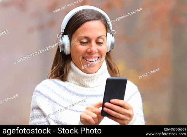 Happy middle age woman wearing headphones listening to music on smart phone