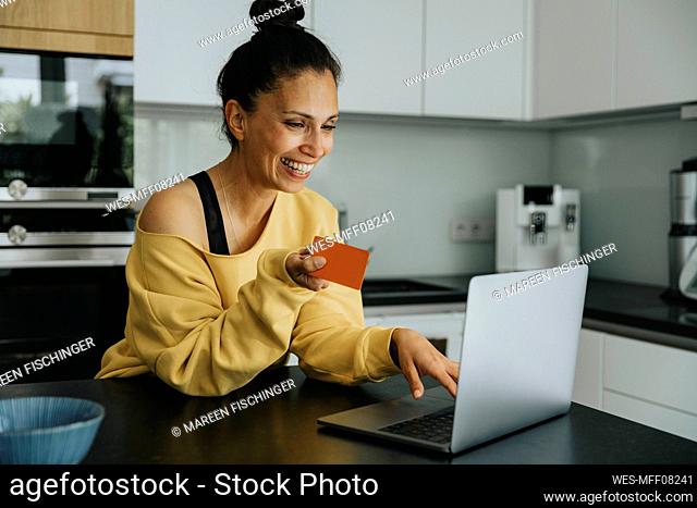 Smiling woman doing online shopping through credit card at kitchen island
