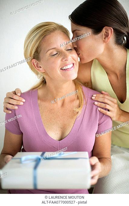 Woman holding gift as girlfriend kisses her cheek