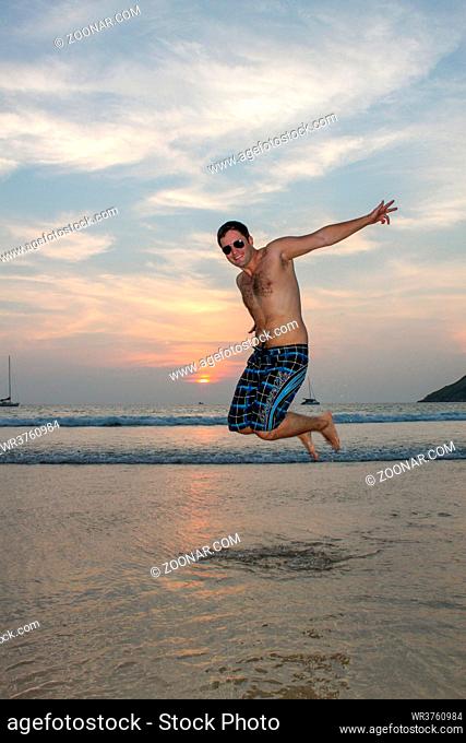 a man jumping happy on the beach with sunset sky in the background