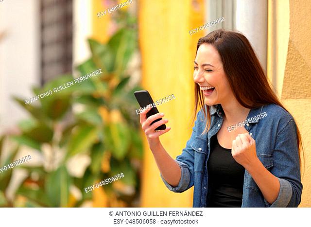 Excited woman finding online offers on a smart phone in the street