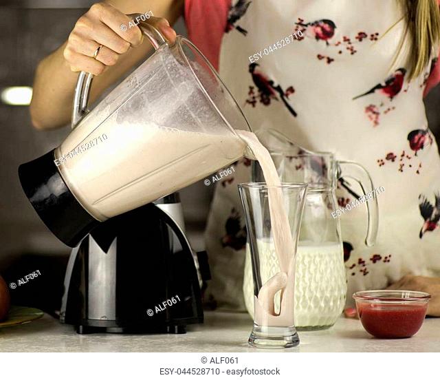 A beautiful woman preparing a milk cocktail with fruits in the kitchen