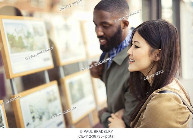 Smiling young couple looking at real estate listings at storefront