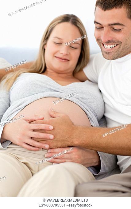 Portrait of future parents feeling their baby while resting on the bed