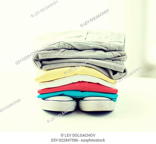 clothes, personal staff and objects concept - close up of folded shirts, pants and shoes on table at home