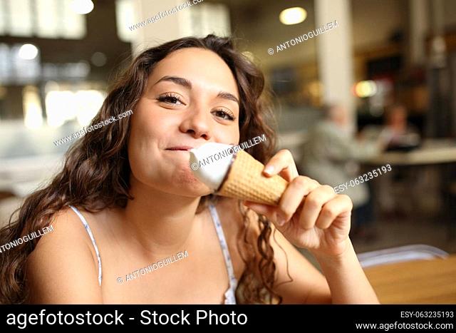 Happy woman eating ice cream looks at you in a coffee shop