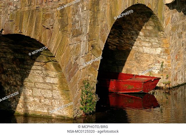 Red rowboat under a bridge