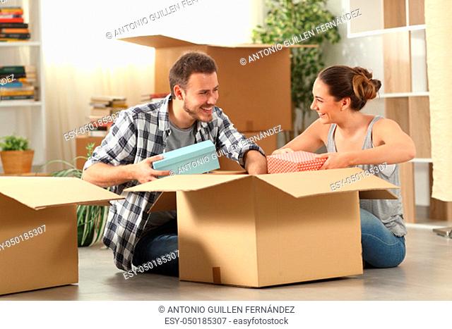 Happy couple unboxing belongings moving house sitting on the floor