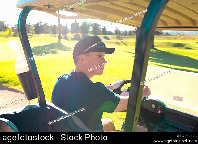 Rear view of caucasian young man wearing cap looking away while driving golf cart in summer