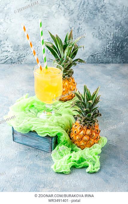 Cocktail with pineapple in two glass glasses with ice and two mini pineapples on a gray background