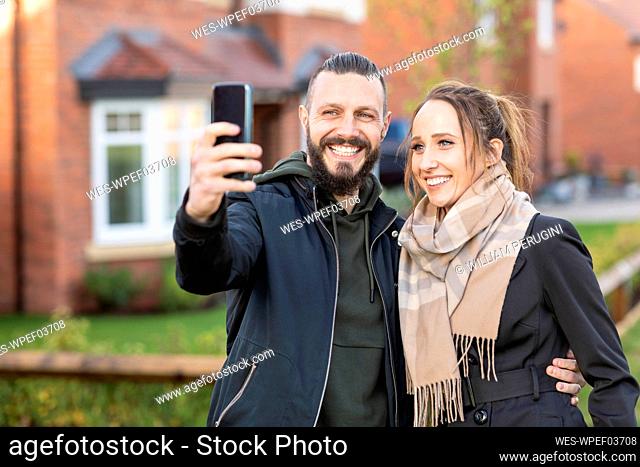 Smiling man taking selfie with girlfriend while standing outside new house