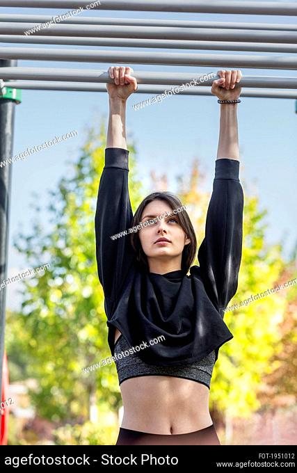 Fit young woman hanging from monkey bars at playground