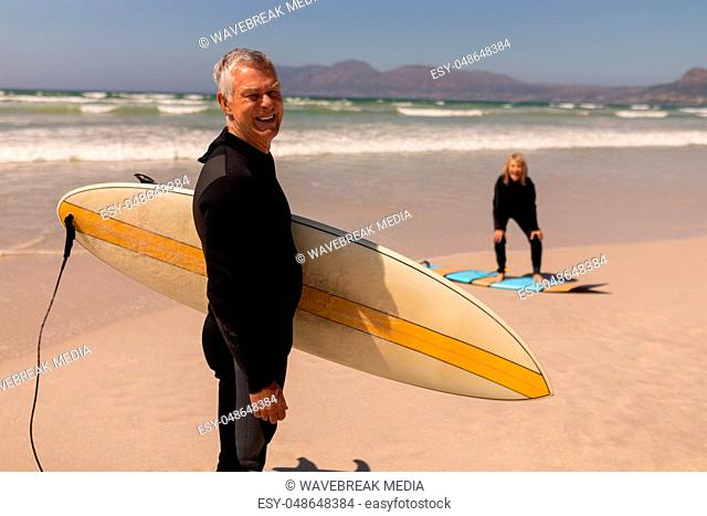 Side view of senior surfer couple standing with surfboard on the beach