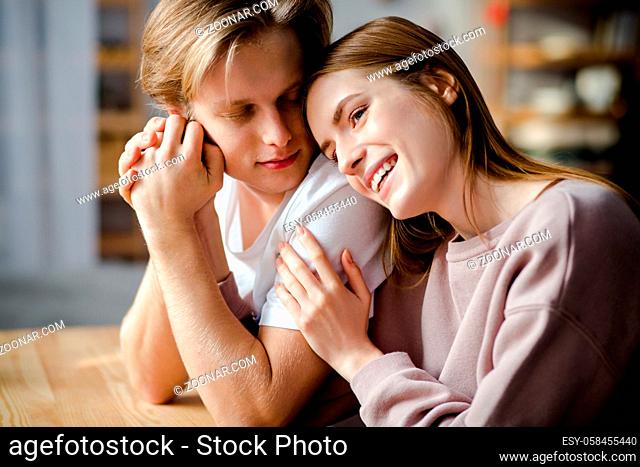 A portrait of two passionate young people. They sit at the table and a girl put her head on her boyfriend shoulder