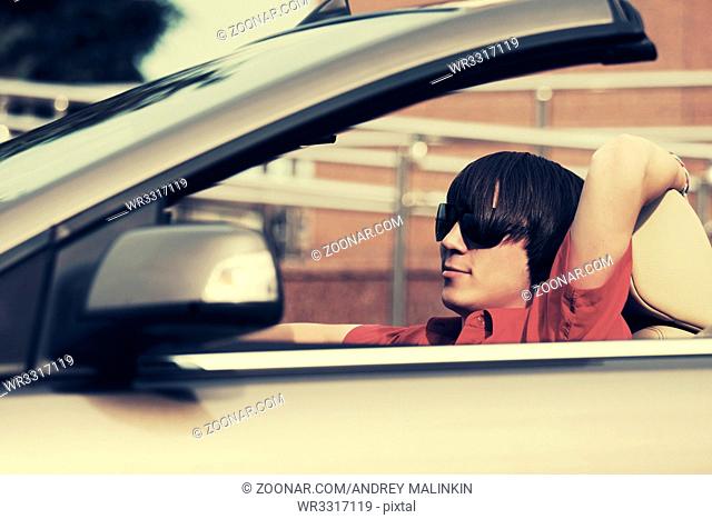 Young man in sunglasses driving convertible car