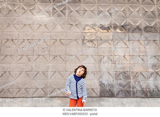 Little boy pulling funny faces in front of concrete wall
