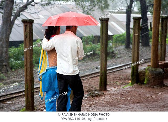 Monsoon ; man and woman walking with holding red umbrella in rain water ; Hill station ; Matheran ; Maharashtra ; India