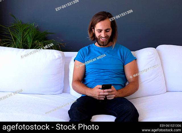Caucasian man sitting on sofa using smartphone and smiling