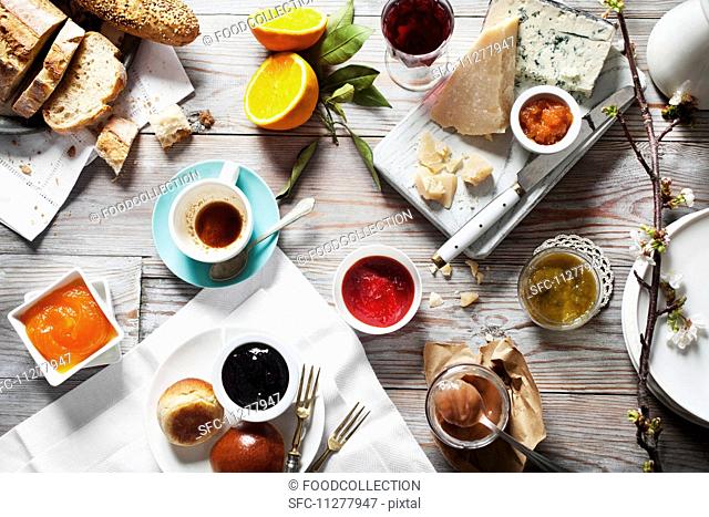 Various types of jam with cheese, bread and drinks on a wooden table