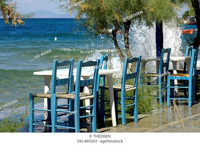tables and chairs of a greek kafenion bar restaurant close by the sea at the shore in Horto peninsula Pilion Thessaly waves splashing against the wall