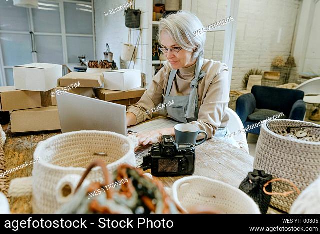 Craftswoman using laptop on workbench in workshop