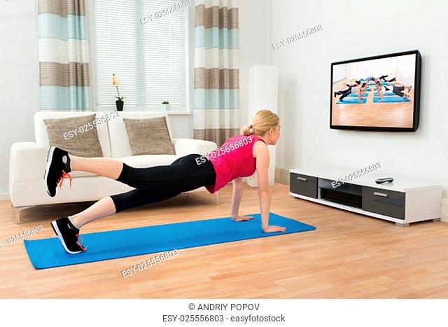 Young Woman Doing Workout While Watching Television In House