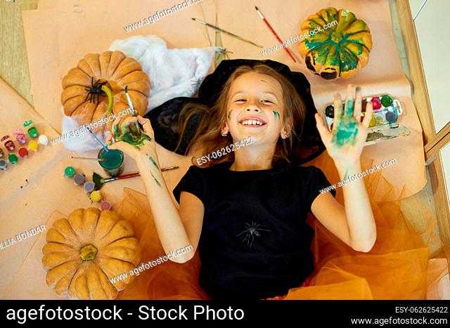 Top view of Smiling girl lying on the floor between drew pumpkin Halloween, and decoration for party, paint hands, emotion, make faces