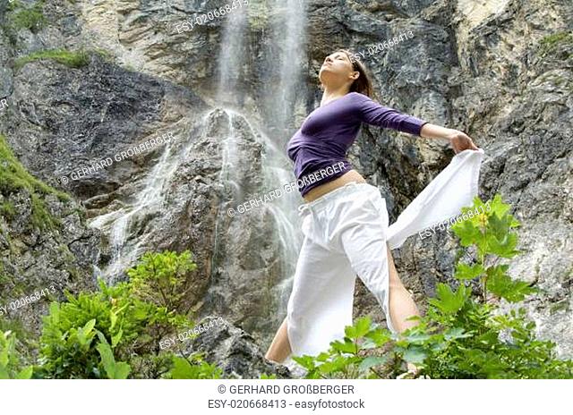 Junge Frau trainiert Übungen vor einem Wasserfall