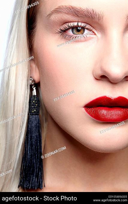 Close-up macro portrait of beauty young woman with black panicle earrings. Blonde female with hand near face on gray studio background