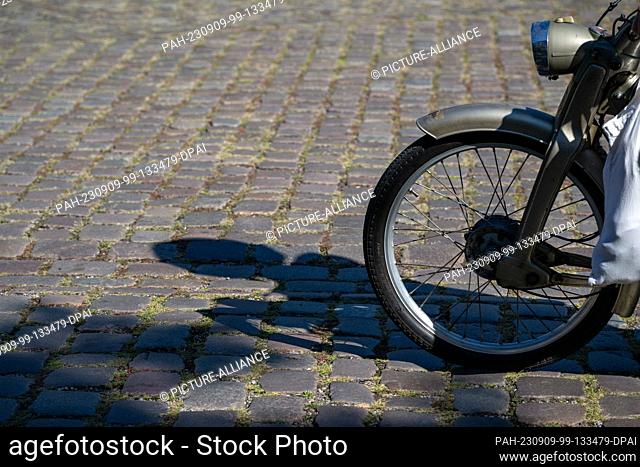 09 September 2023, Bavaria, Lohr Am Main: A two-wheeler rider casts his shadow on the cobblestones in the blazing midday sun
