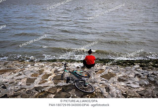 29 July 2018, Germany, Wilhelmshaven: A woman sits with headphones on the southern beach at the North Sea. Photo: Mohssen Assanimoghaddam/dpa