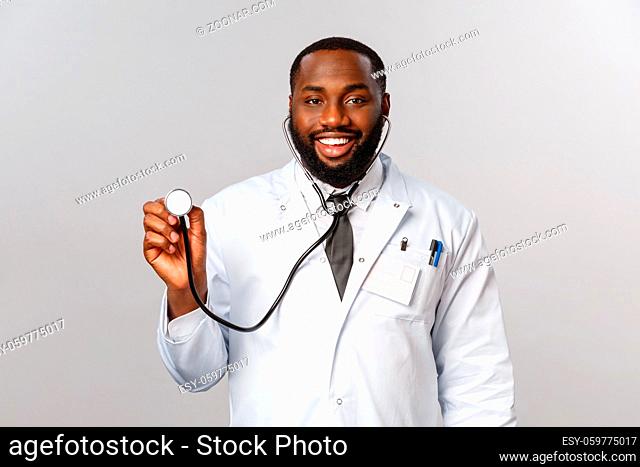 Covid19, hospital check-up and healthcare concept. Handsome african-american doctor, physician came to patient with stethoscope treating coronavirus symptoms...