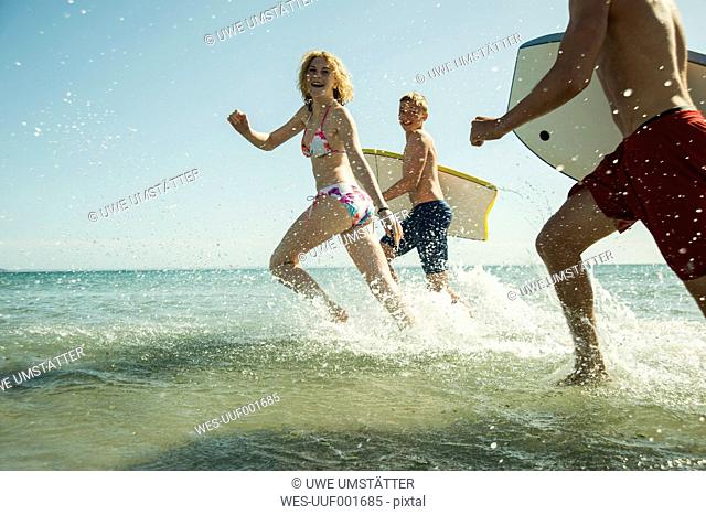 Three teenagers with surfboards running at waterside of the sea