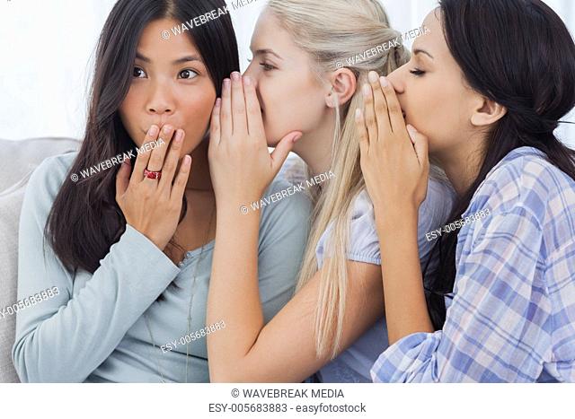 Two friends whispering secrets to shocked brunette